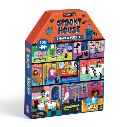 The Spooky House 100 Pc House-Shaped Puzzle by Stephanie Birdsong features cartoon haunted house scenes with skeletons, ghosts, bats, black cats, and monsters in Halloween-themed rooms—perfectly packed in a colorful box.