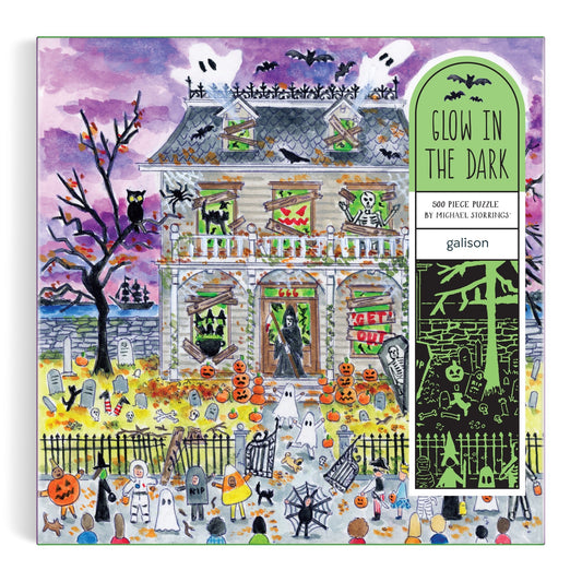 The Michael Storrings Haunted House 500 Piece Glow in the Dark Puzzle features a Halloween scene with ghosts, pumpkins, bats, skeletons, and costumed trick-or-treaters under a purple sky—perfect for intermediate puzzlers.