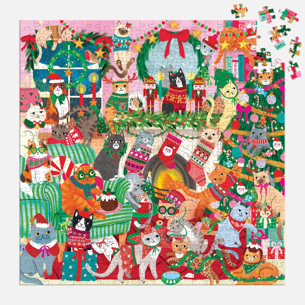 The Merry Catmas! 500 Piece Family Puzzle by Rebecca Jones features colorful cats indoors, wearing sweaters or hats, amidst festive decorations, wreaths, stockings, gifts, and trees for a cheerful holiday scene.
