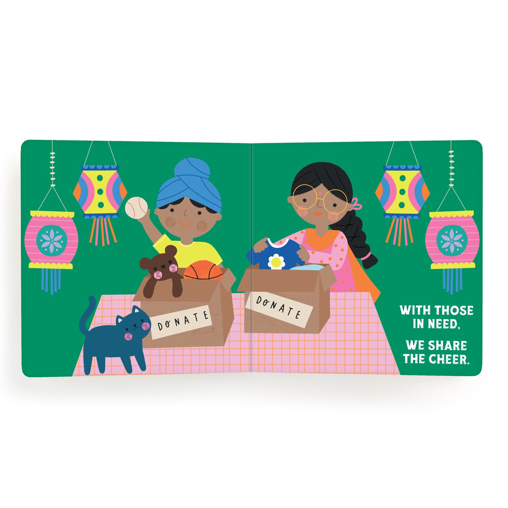Two women pack clothes, toys, and food into donation boxes at a table while a black cat watches. Colorful lanterns glow above for Diwali. Text reads: With those in need, we share the cheer. Inspired by Lets Celebrate Diwali Board Book by Nina Ghataora.