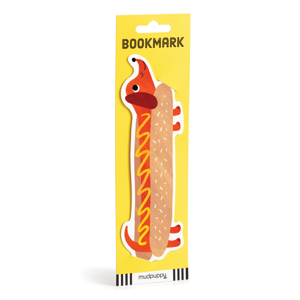 A playful page-keeper for bookworms, the Hot Dog Bookmark showcases a dachshund dressed as a hot dog with mustard on yellow packaging labeled BOOKMARK. The Rebecca Jones brand name appears at the bottom.