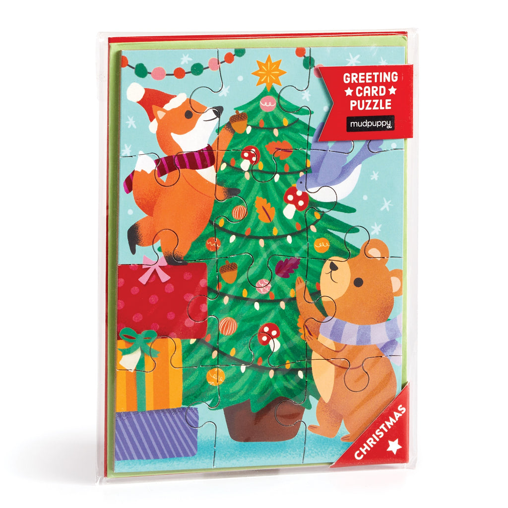 The Christmas Critters Greeting Card Puzzle by Ana Peake features a fox and bear in scarves decorating a tree with gifts. Festive and fun, its ideal for holiday entertainment. Packaging reads Greeting Card Puzzle and Christmas.