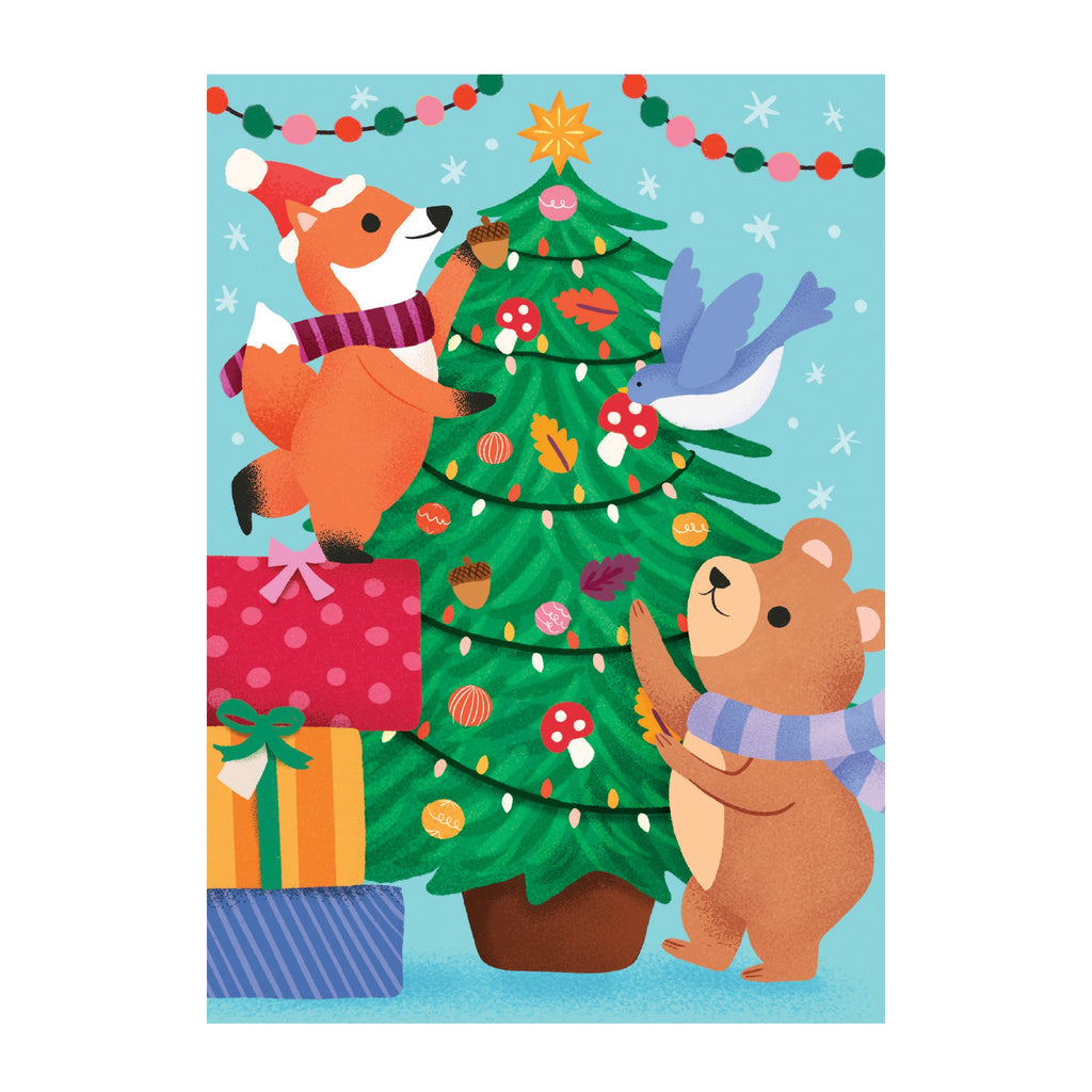 The Ana Peake Christmas Critters Greeting Card Puzzle features a fox and bear in winter scarves decorating a tree with ornaments, while a bluebird, colorful presents, festive lights, and garlands complete the holiday scene.