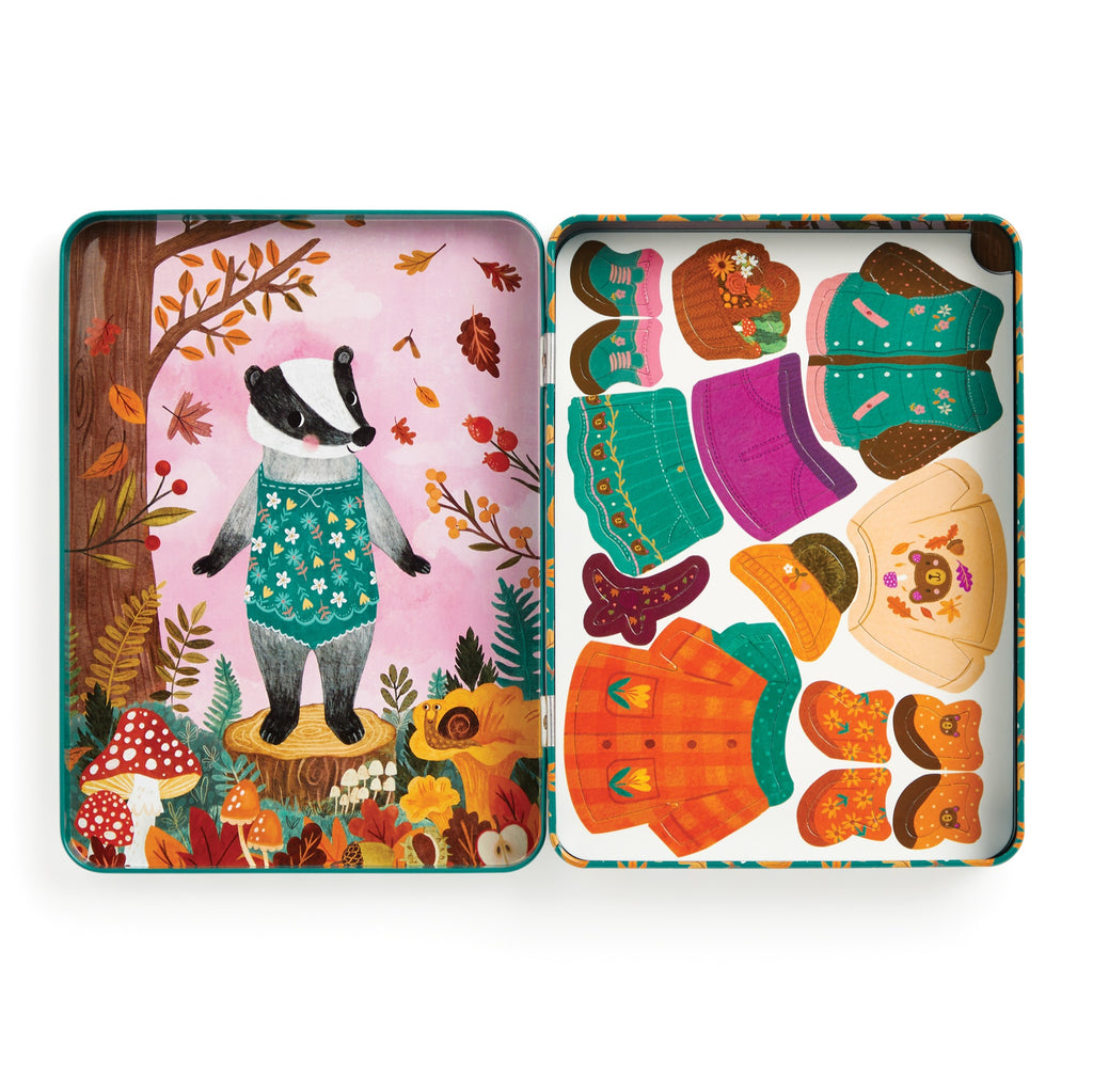 The Jenny Miriam Hughes Folklore Forest Magnetic Dress-up Play Set features a badger in teal overalls among autumn leaves and mushrooms, plus fairy tale hats, boots, sweaters, and dresses, all organized in a handy tin.