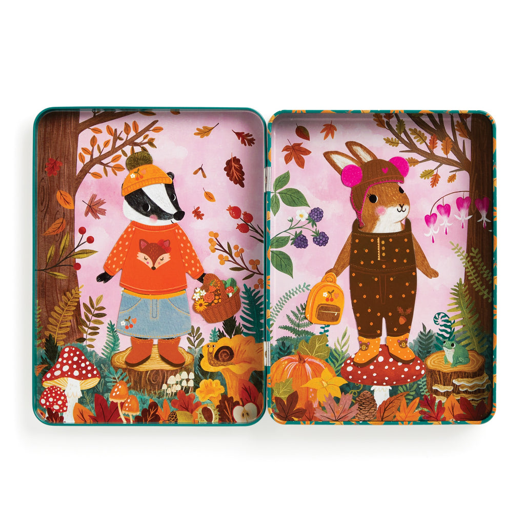 The Folklore Forest Magnetic Dress-up Play Set by Jenny Miriam Hughes features a badger and guinea pig in autumn outfits with fairy tale accessories on tree stumps, surrounded by leaves, mushrooms, flowers, and berries on a pink background.