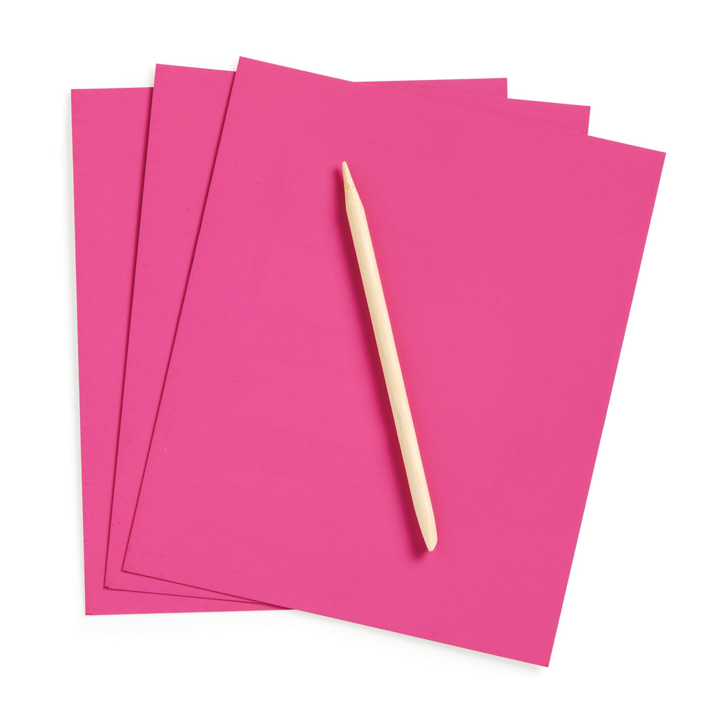 Three bright pink sheets from Katie Woods Unicorn Glam Scratch Magic are stacked and slightly overlapping, with a wooden stylus placed diagonally on top, all set against a white background.